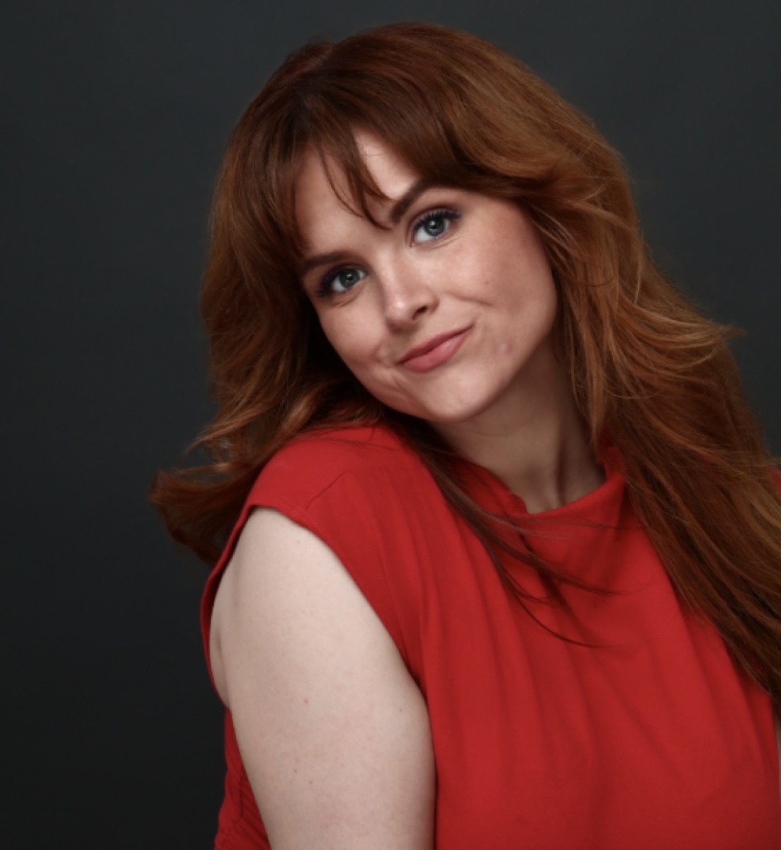 Blaire Erskine shrugging playfully in a red top.
